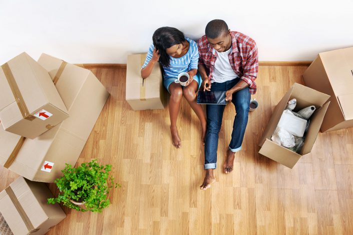 overhead view of young couple with moving boxes in new apartment using modern tablet computer technology